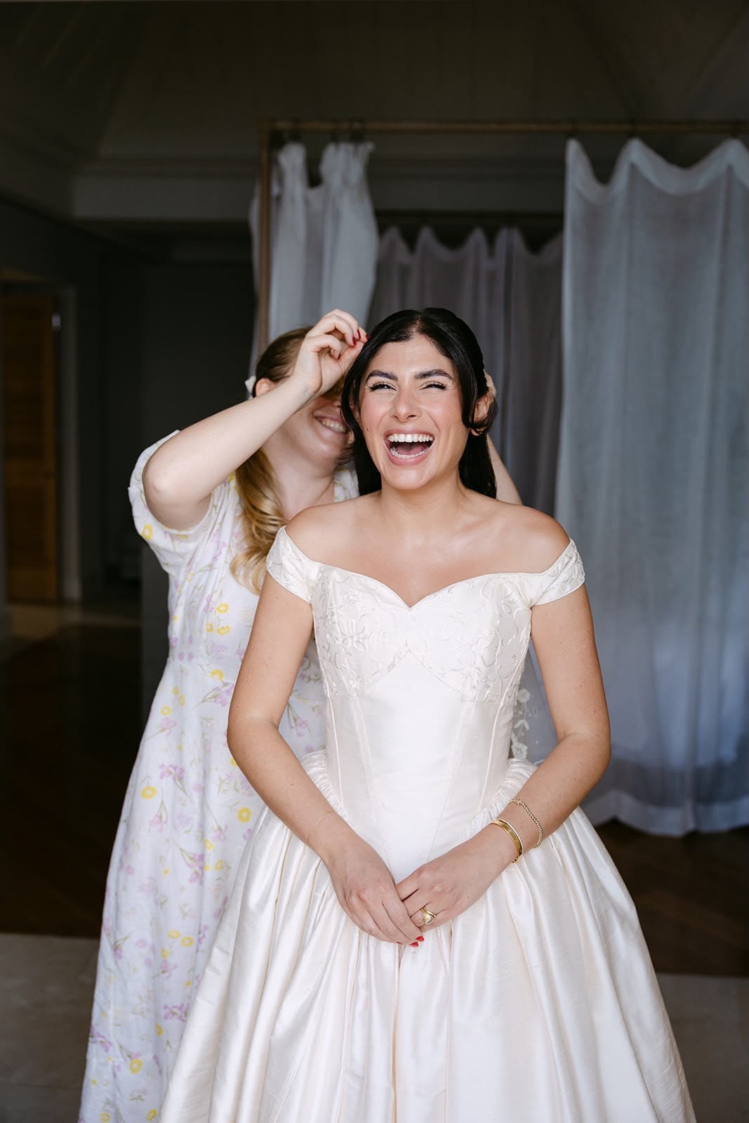 Bride laughing while a friend adjusts her hair
